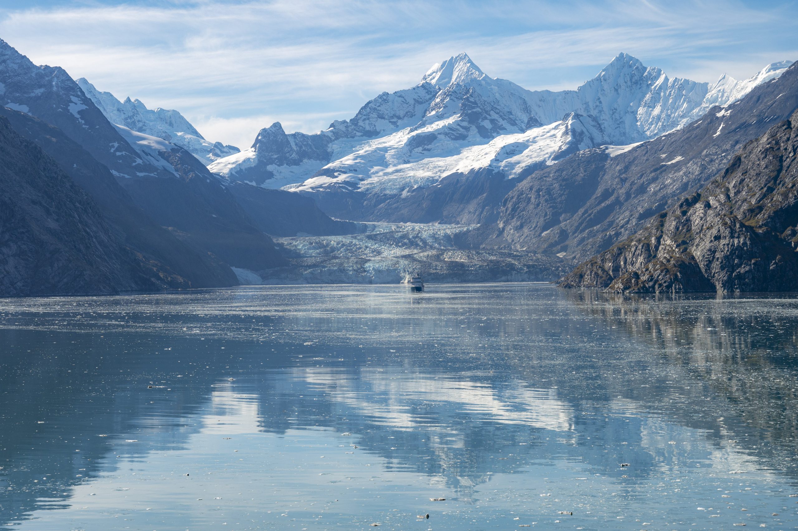 Distant view of mountains and glacier in the center of a fjord. A large cruise ship sits in front of the glacier.